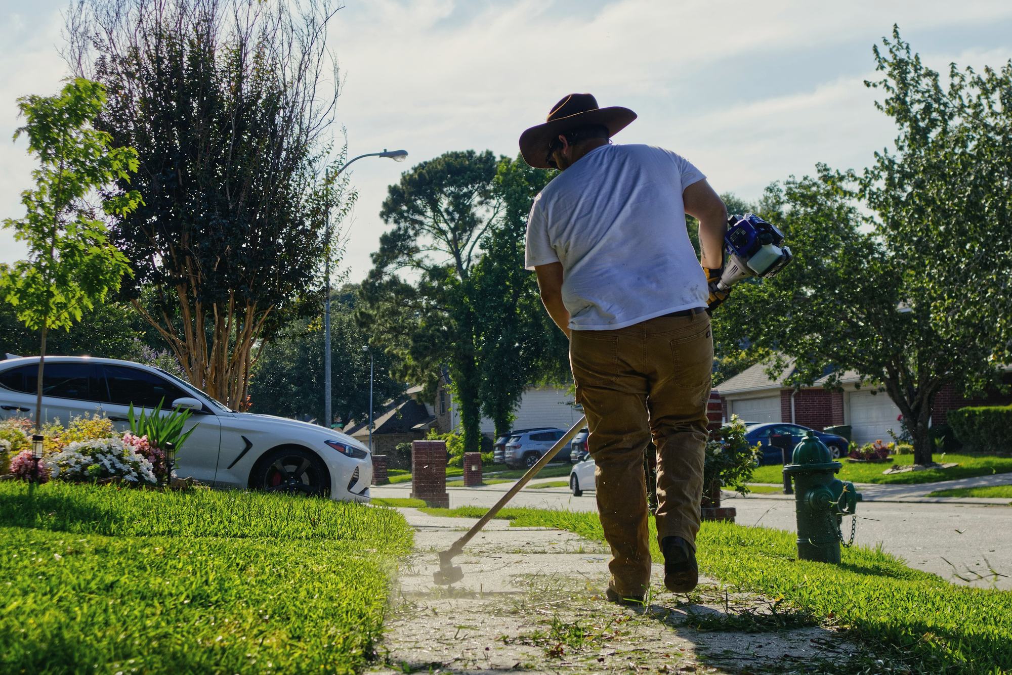 A crew member edging a front walk with a string trimmer on a residential street
