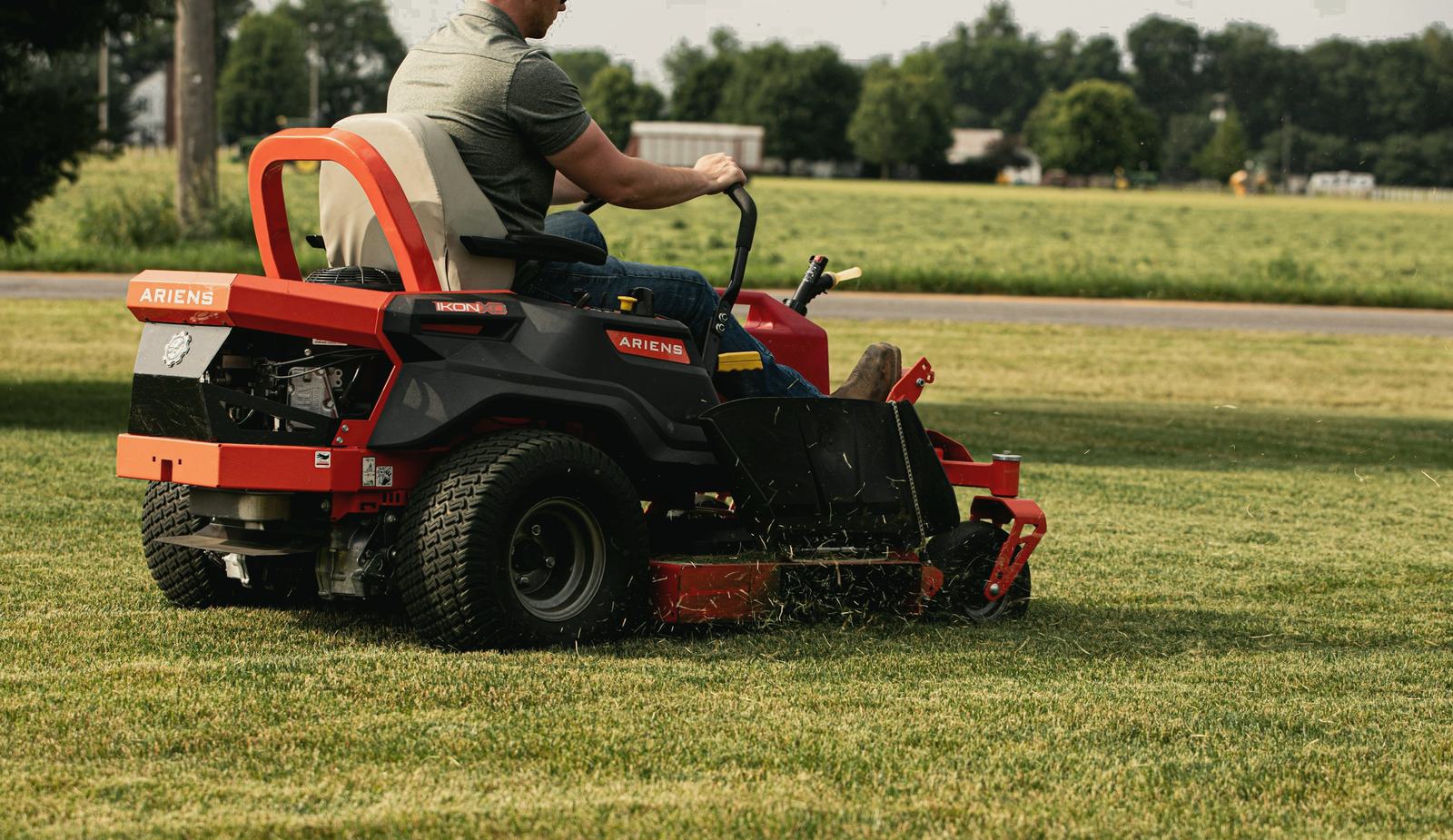 A crew member on a zero-turn mower cutting a wide lawn